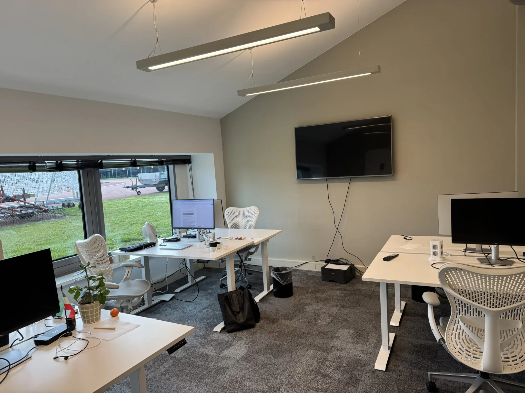 Moderne kantoorruimte 0.09 met bureaus, computerschermen, ergonomische stoelen en een groot scherm aan de wand.