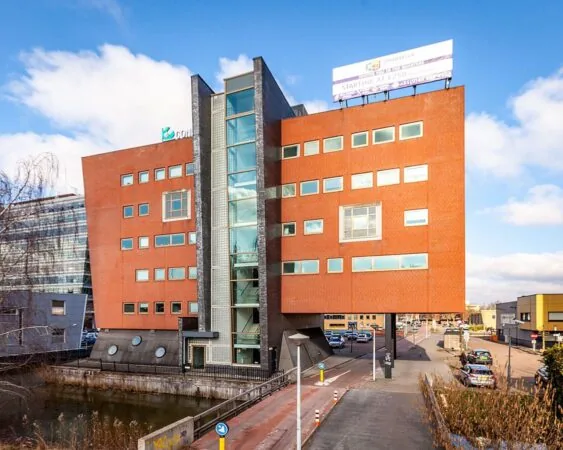 Modern rood bakstenen kantoorgebouw met glazen trappenhuis en opvallend overhangend ontwerp aan een waterkanaal.