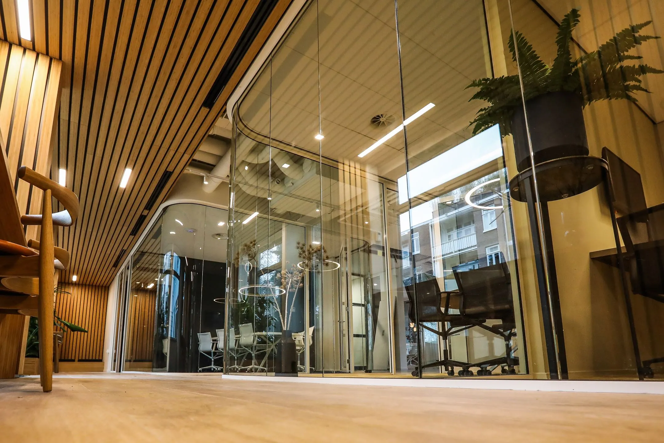 Moderne kantoorruimte met glazen wanden, houten plafond en vergaderruimtes met designmeubilair.