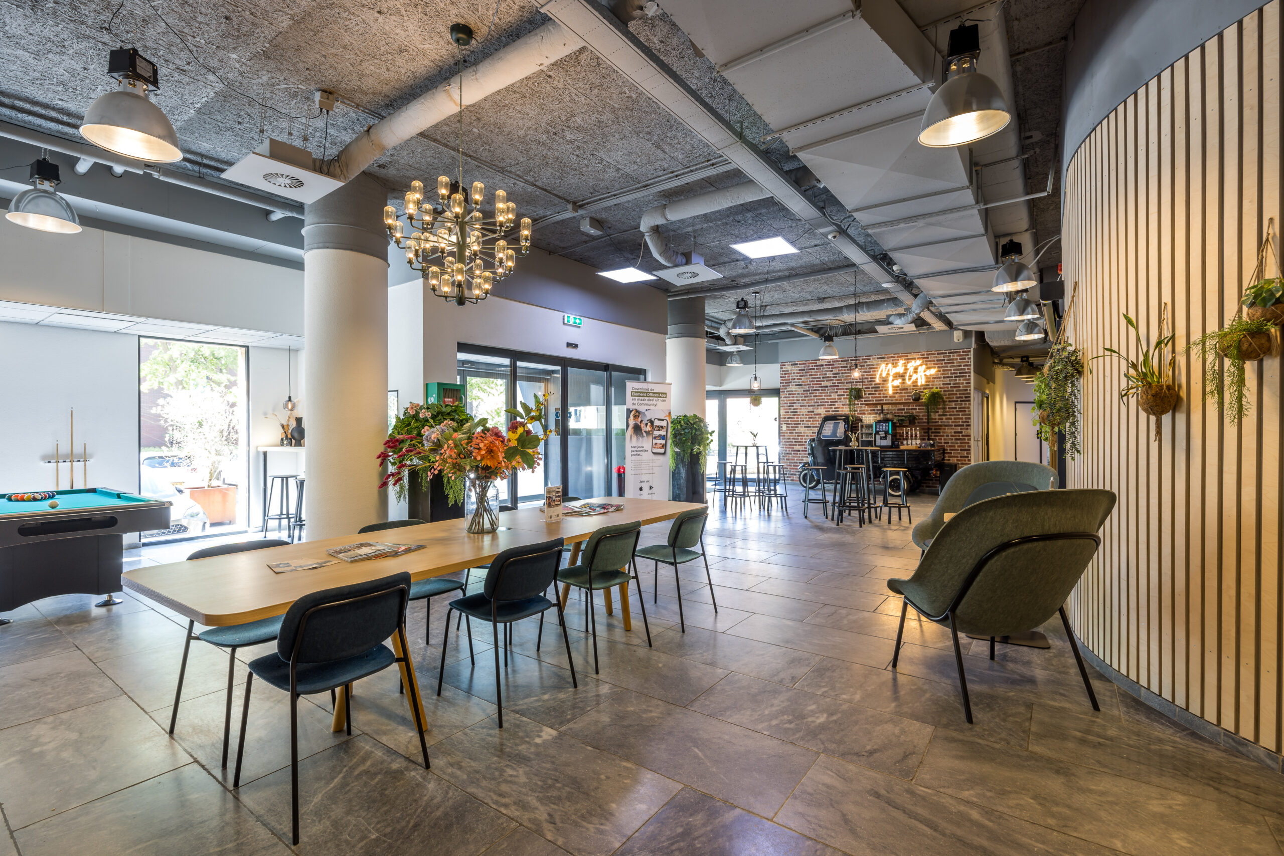 Interieur van een modern kantoor met een lange tafel, planten, een kroonluchter en een tafeltennistafel.