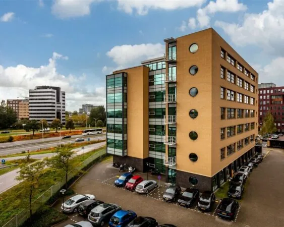 Modern kantoorgebouw 020_1440 met parkeerplaatsen, gelegen aan een drukke weg in een stedelijke omgeving.