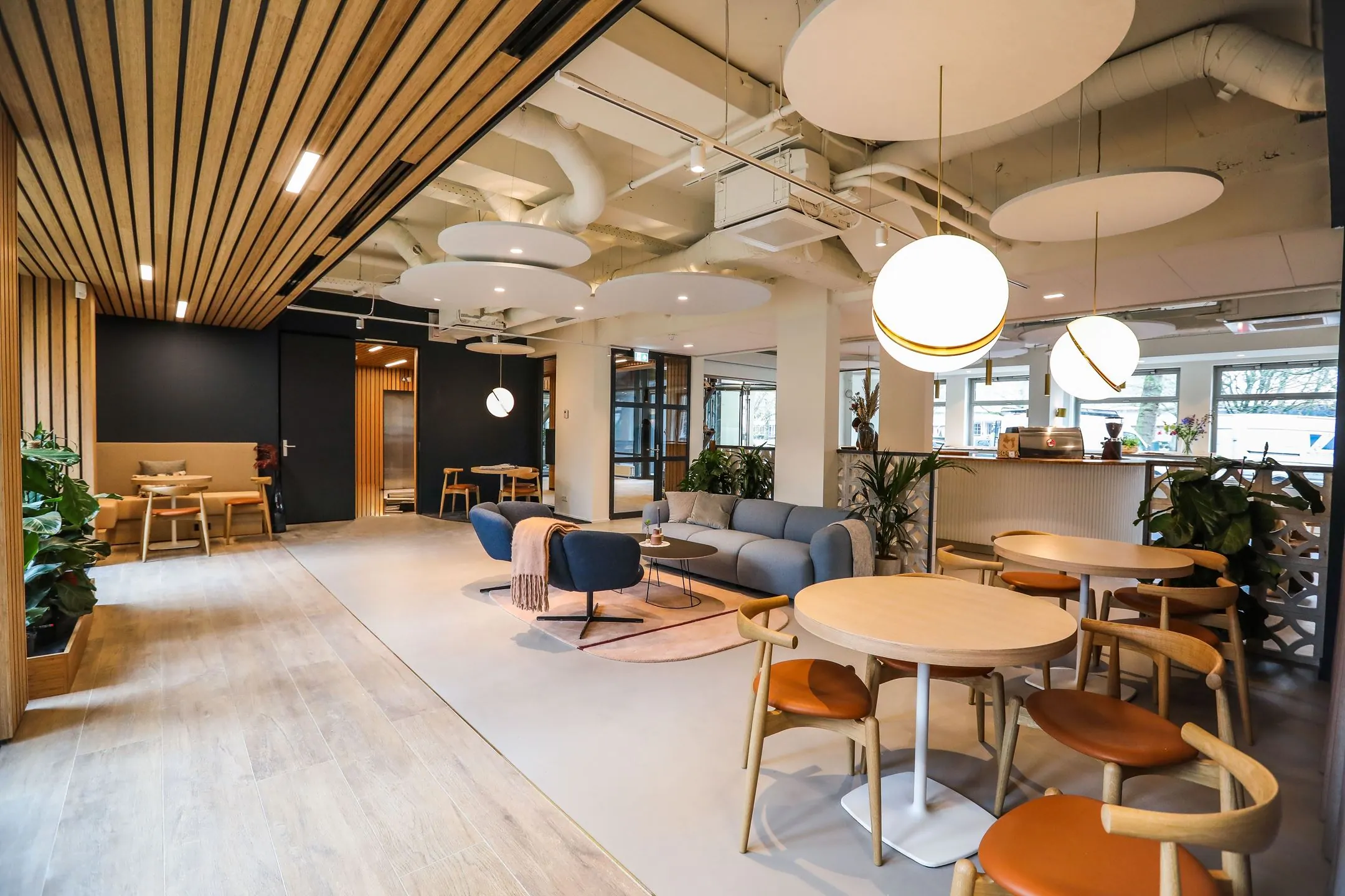 Modern ingerichte lounge- en werkruimte met ronde tafels, comfortabele zitplekken en warme houten accenten, getiteld 020_2160.