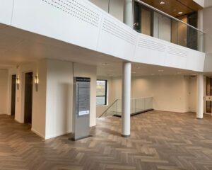 Moderne en lichte entreehal met houten visgraatvloer, liften, glazen balustrade en informatiezuil in gebouw 022_2160.