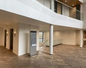 Moderne en lichte entreehal met houten visgraatvloer, liften, glazen balustrade en informatiezuil in gebouw 022_2160.