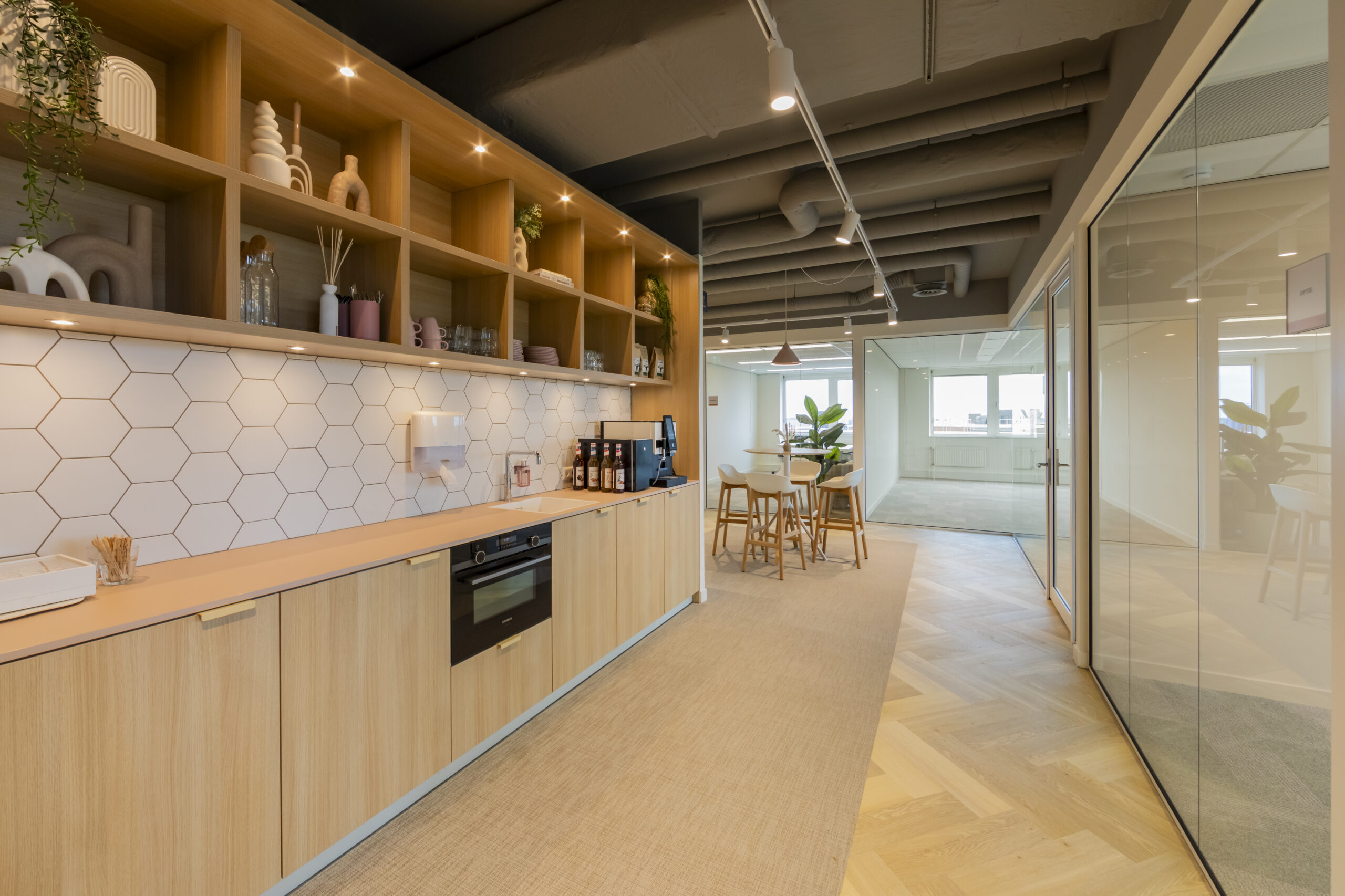 Moderne kantoorruimte met houten keuken, hexagon-tegelwand en vergadertafel in een lichte omgeving.