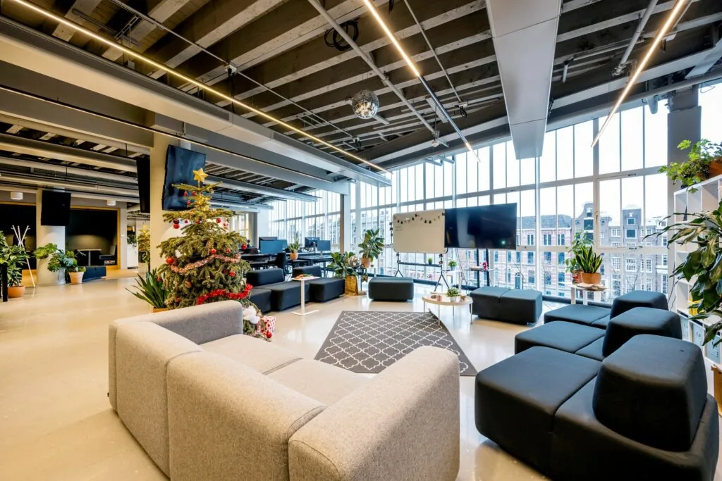Moderne kantoorruimte met grote ramen, een kerstboom en een gezellige zithoek met planten en schermen.