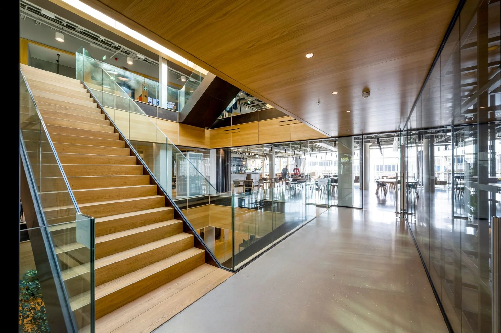 Moderne kantoorruimte met een brede houten trap, glazen wanden en een open werkruimte op de achtergrond.