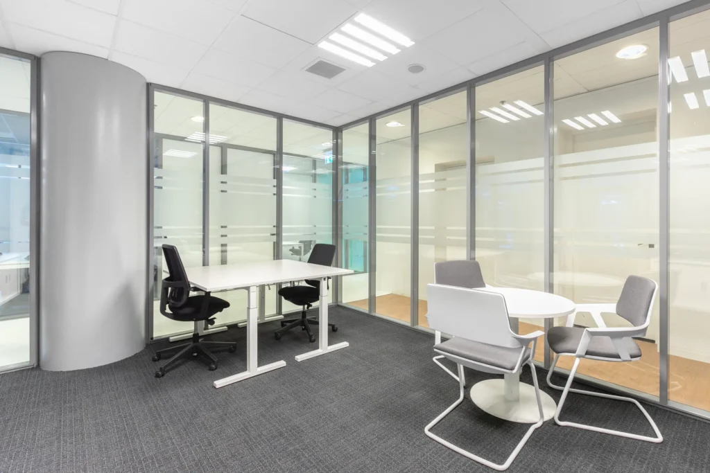 Moderne kantoorruimte met glazen wanden, een bureau met stoelen en een ronde tafel met stoelen.