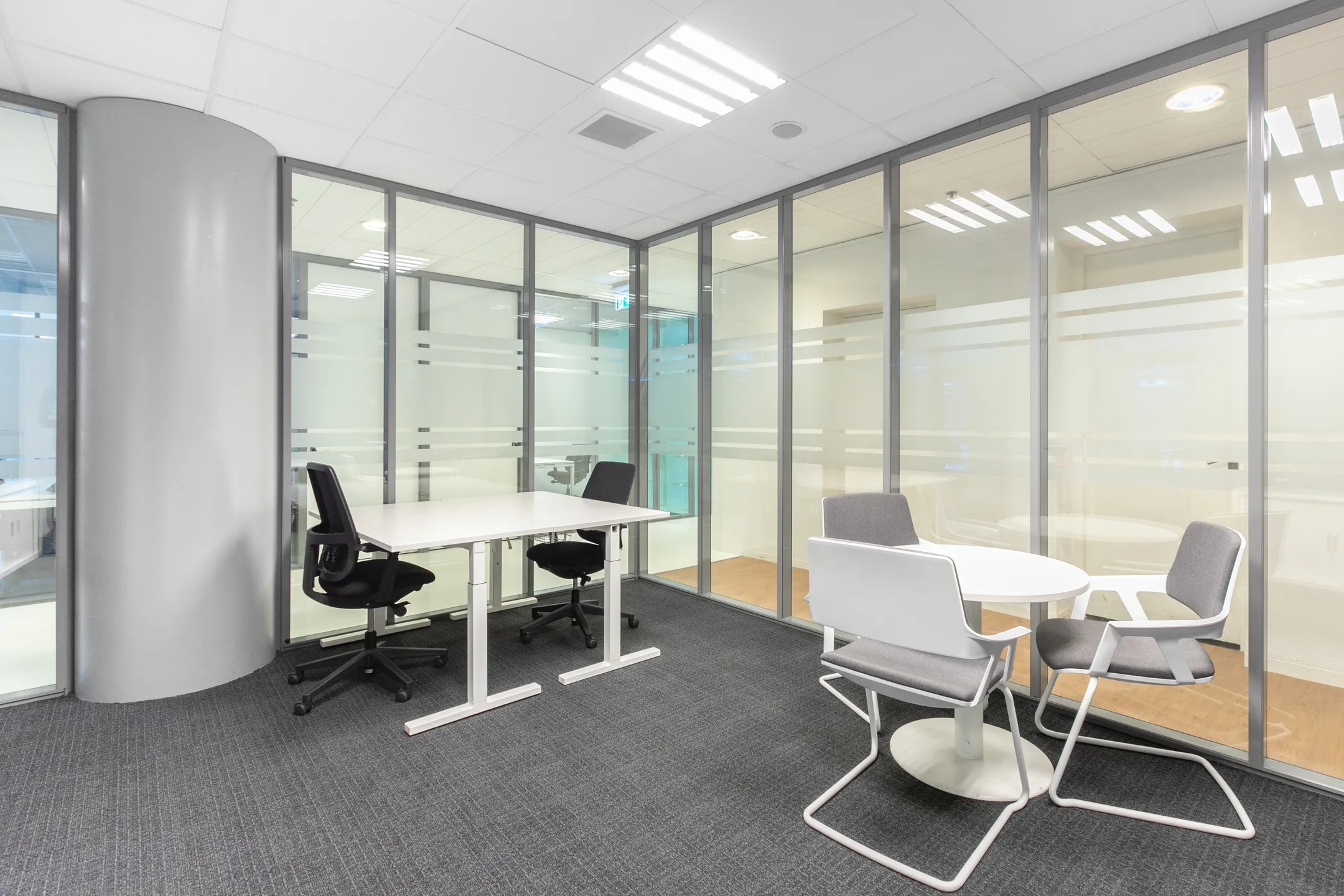 Moderne kantoorruimte met glazen wanden, een bureau met stoelen en een ronde tafel met stoelen.