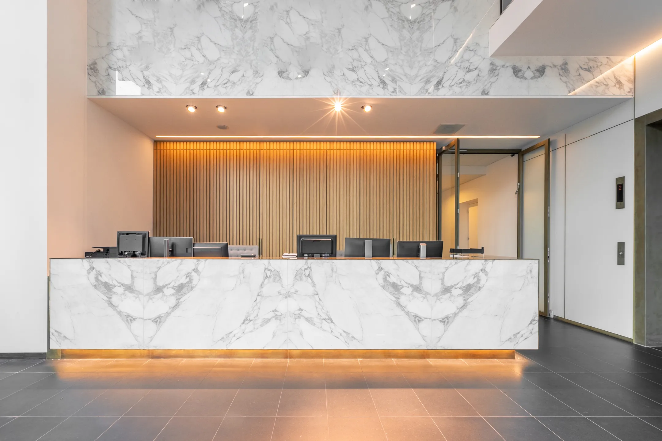 Moderne receptiebalie met marmeren afwerking en strakke houten achterwand.