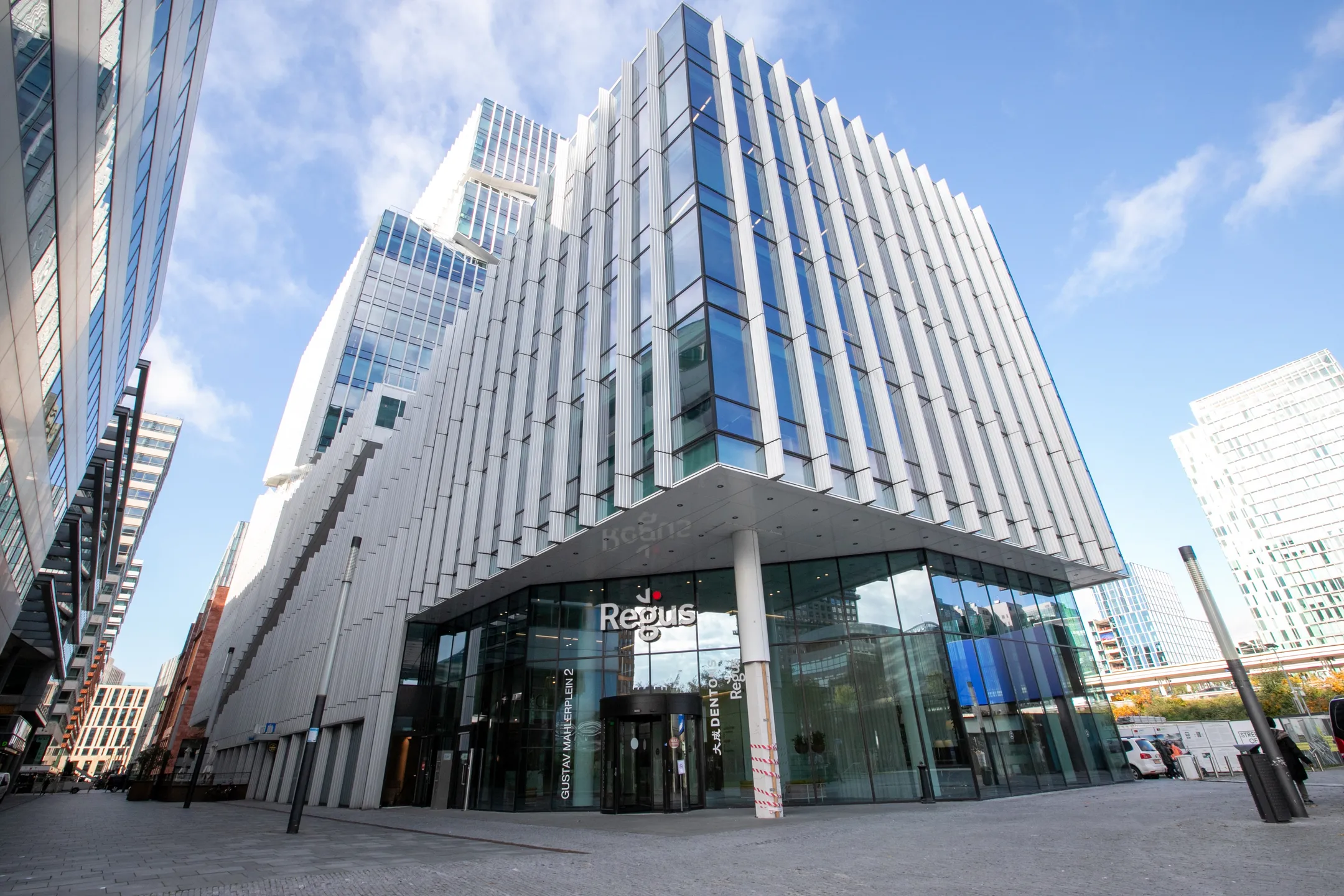 Een modern kantoorgebouw met veel glas en geometrische lijnen onder een blauwe lucht.