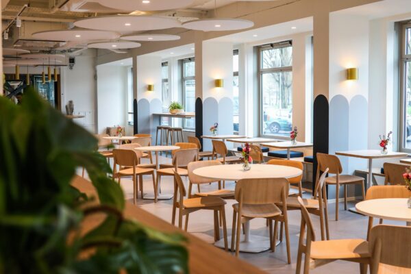 Moderne, licht ingerichte horecaruimte met houten tafels en stoelen, ingericht met kleine bloemenvaasjes.