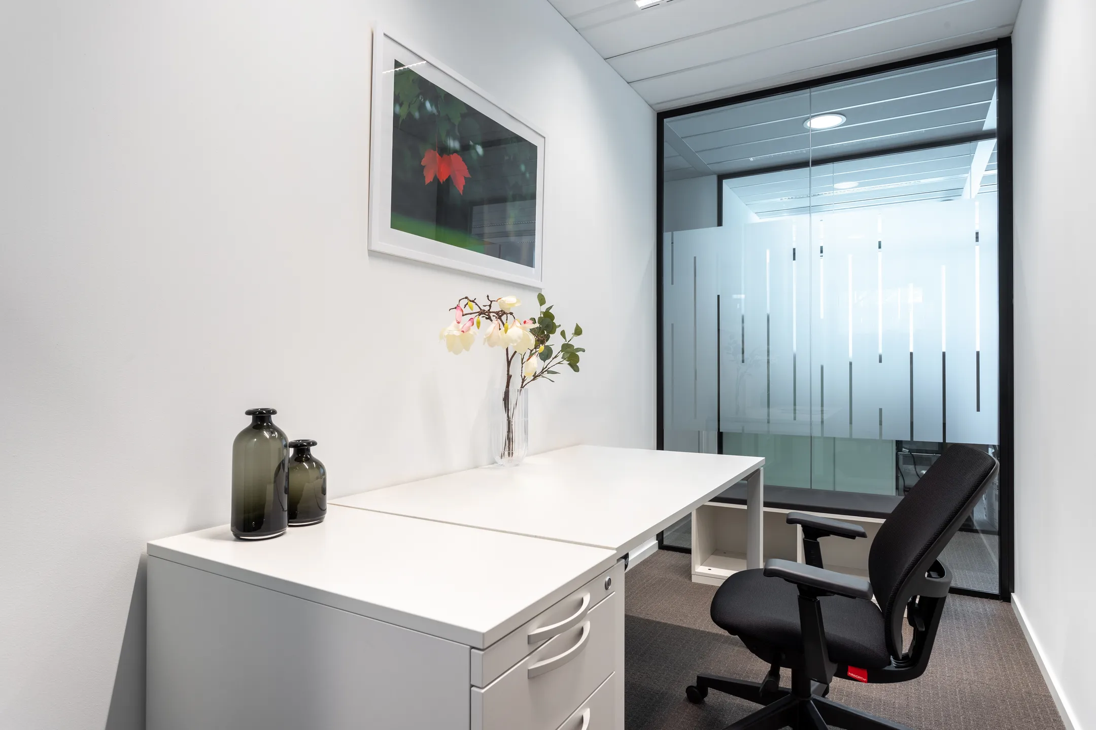 Een minimalistisch ingericht kantoor met een wit bureau, een zwarte bureaustoel en decoratieve vazen.