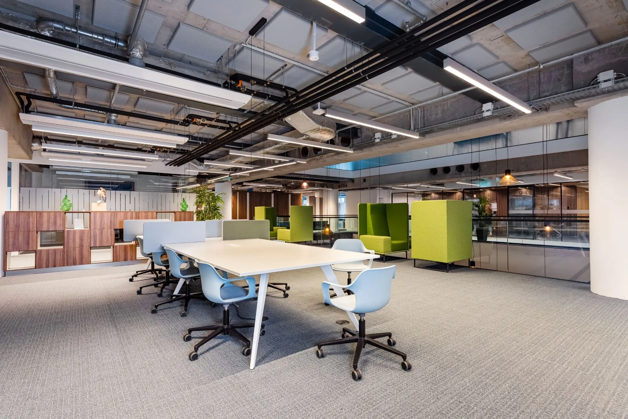 Moderne open kantoorruimte met flexibele werkplekken, groene akoestische stoelen en een industrieel plafond.
