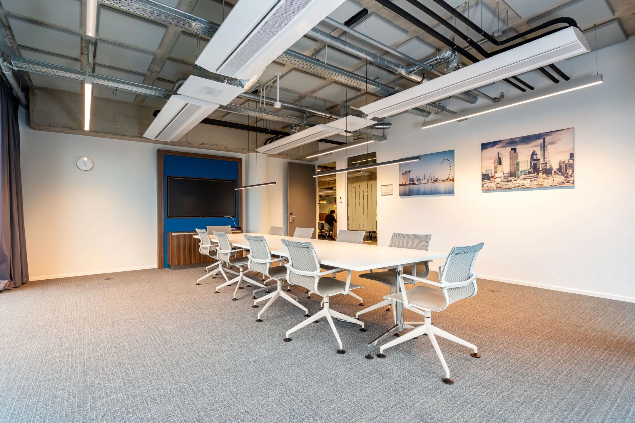 Moderne vergaderruimte met een lange tafel, ergonomische stoelen, een flatscreen en stadsfoto’s aan de muur.