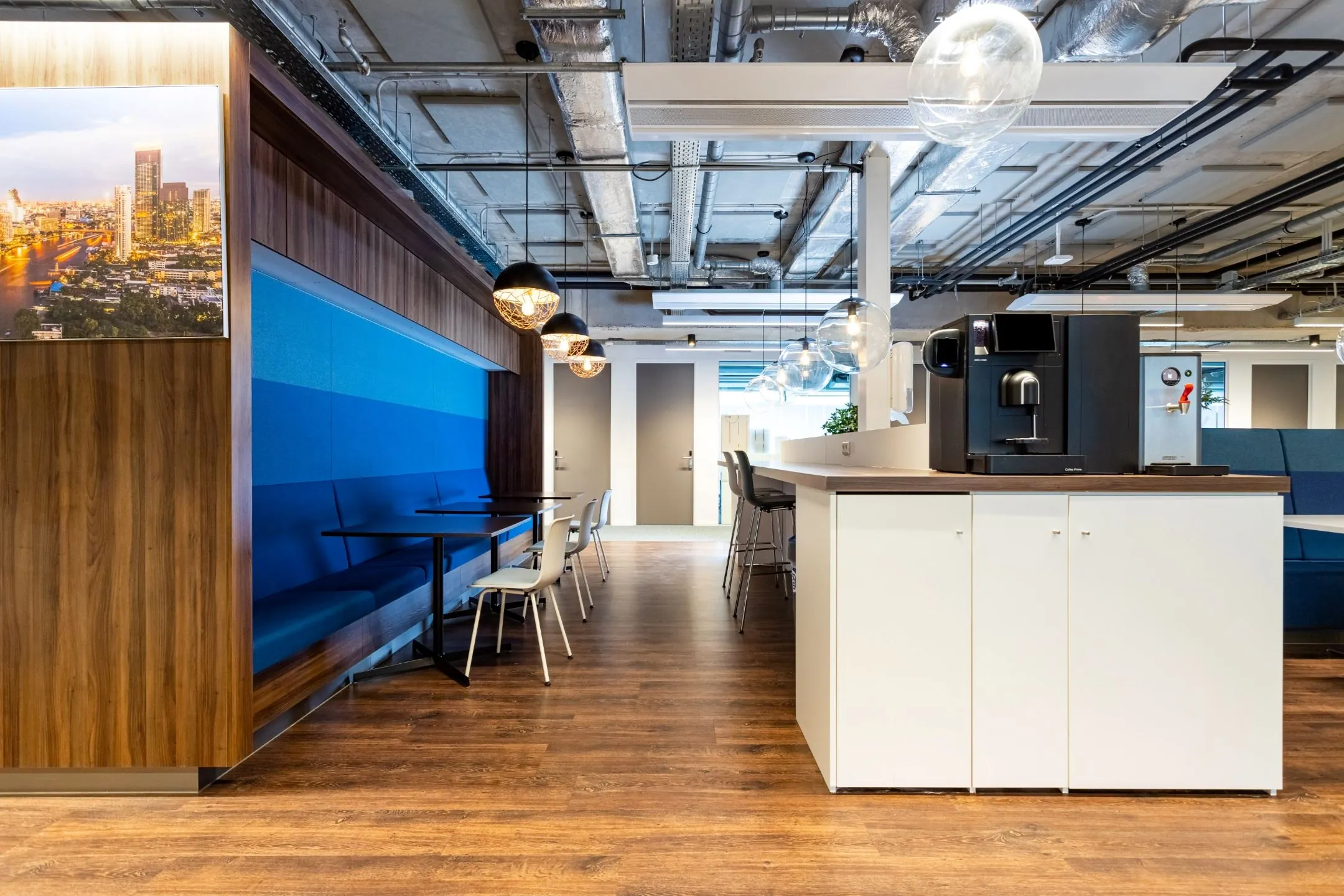 Moderne kantoorlounge met zithoeken, koffiemachine en houten vloer.