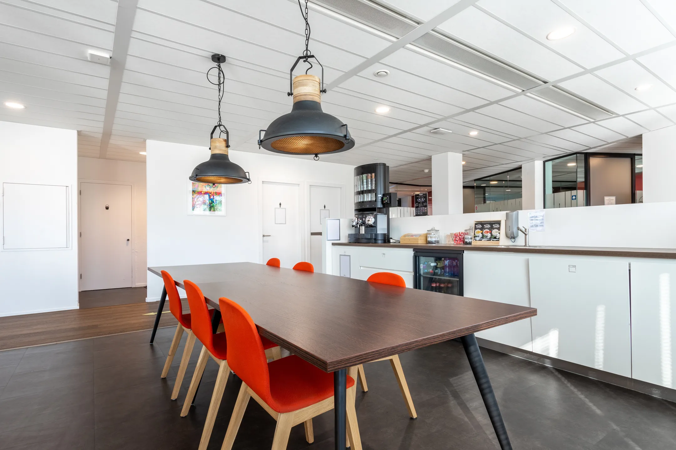 Moderne kantoorruimte met een donkere tafel en feloranje stoelen, verlicht door hangende lampen.