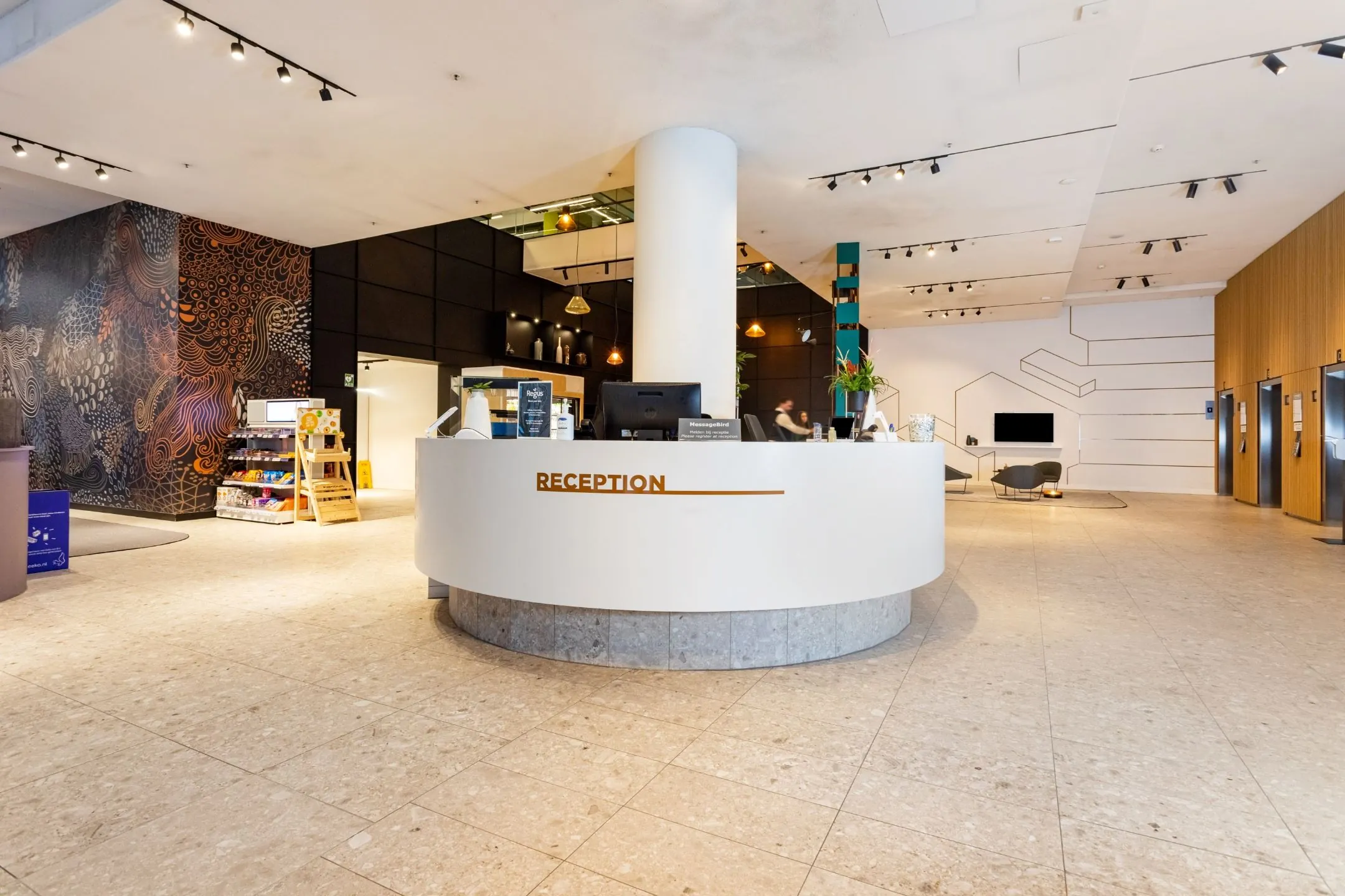 Moderne hotelreceptie met ronde balie, kunstzinnige muurdecoratie en zithoek op de achtergrond.