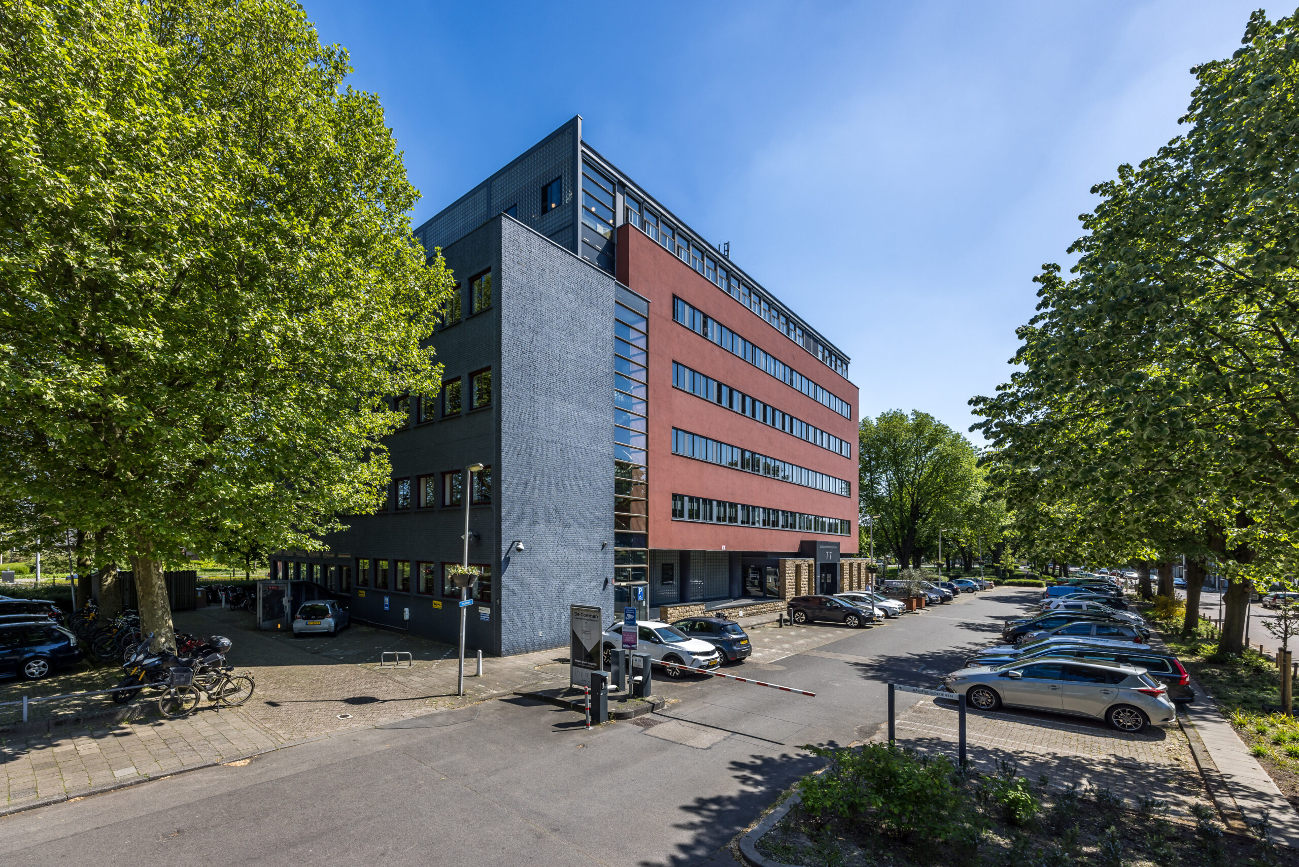 Een kantoorgebouw aan de Goeman Borgesiuslaan 77 in Utrecht, omgeven door een parkeerplaats en bomen.