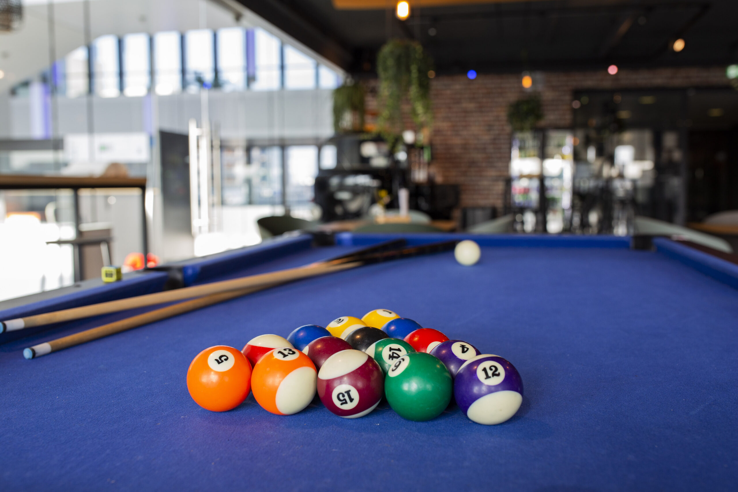 Een biljarttafel met kleurrijke biljartballen en keuen in een moderne kantooromgeving.