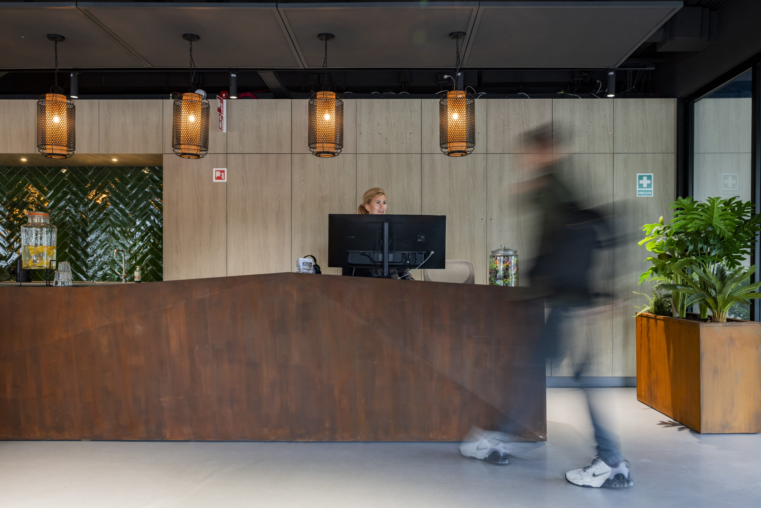 Een receptie met een medewerker achter de balie en een voorbijlopende persoon, omgeven door moderne decoratie.