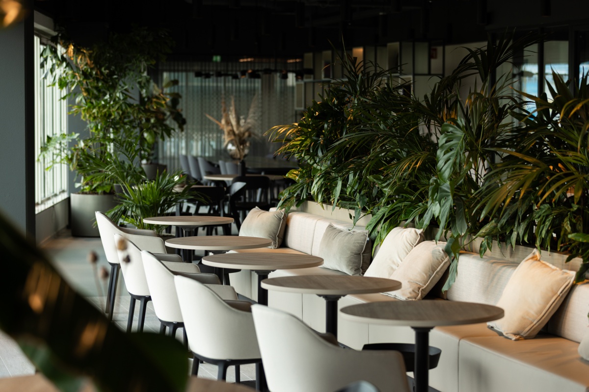 Een sfeervol restaurantinterieur met moderne zitplaatsen en veel groene planten.