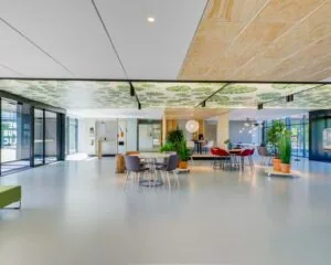 Moderne, open kantoorruimte met zithoeken, veel planten en een plafond bedrukt met groene bladeren.