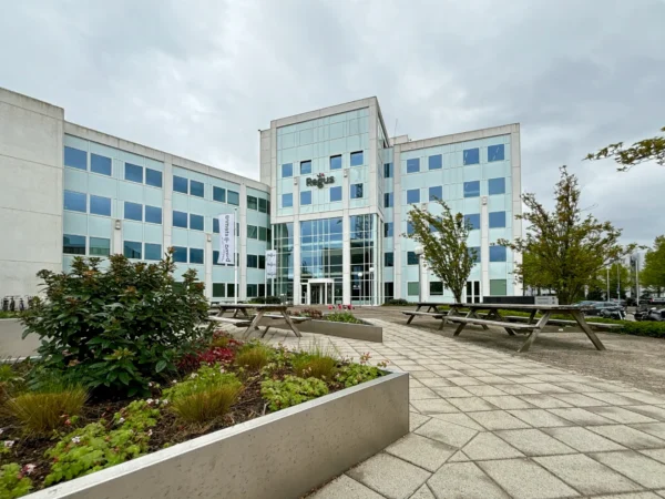 Een moderne bedrijfsgebouw met glazen gevel en omringende groenvoorzieningen.