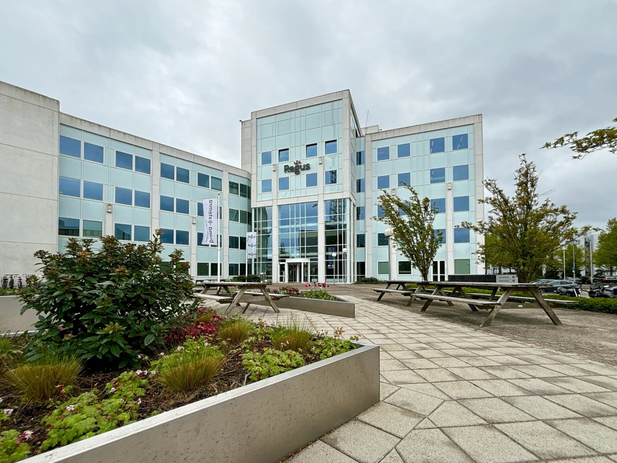 Een moderne bedrijfsgebouw met glazen gevel en omringende groenvoorzieningen.