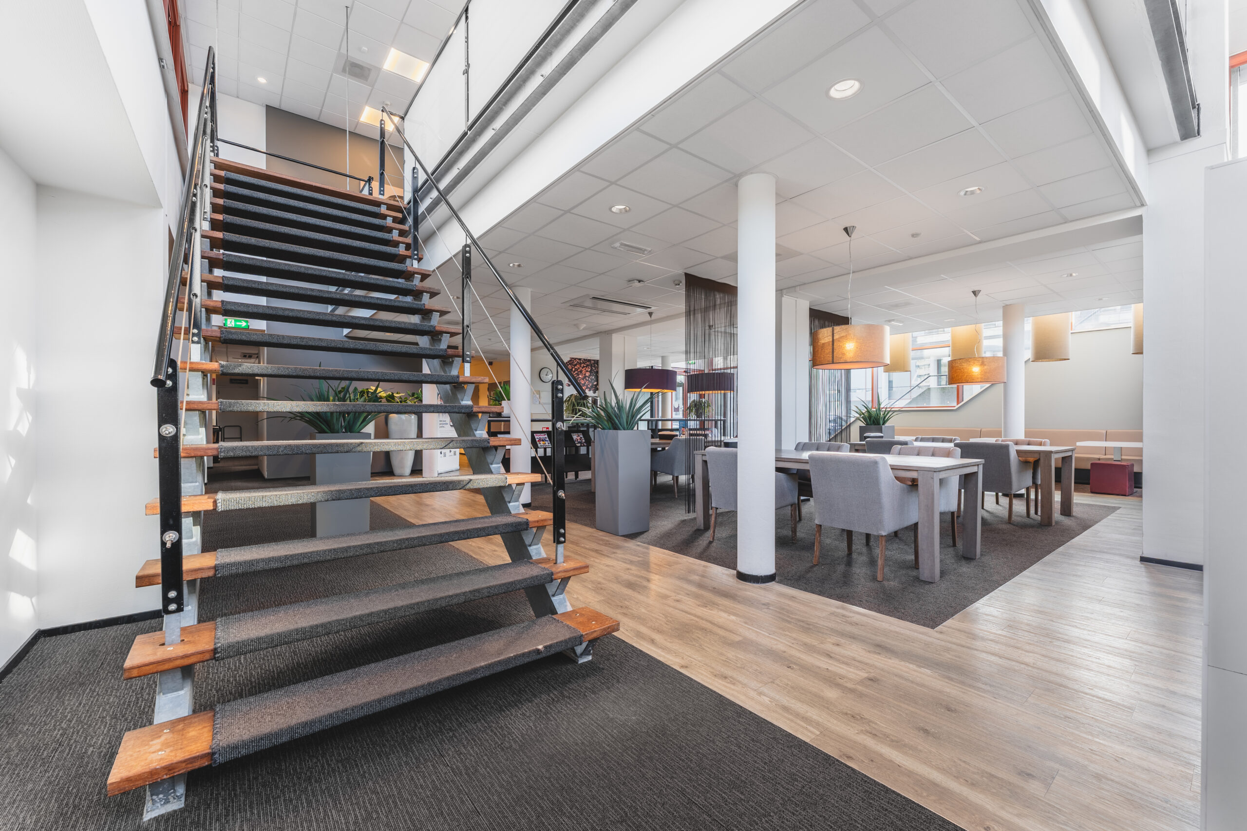 Een moderne kantoorruimte met een brede trap, tafels en stoelen, en veel natuurlijk licht.