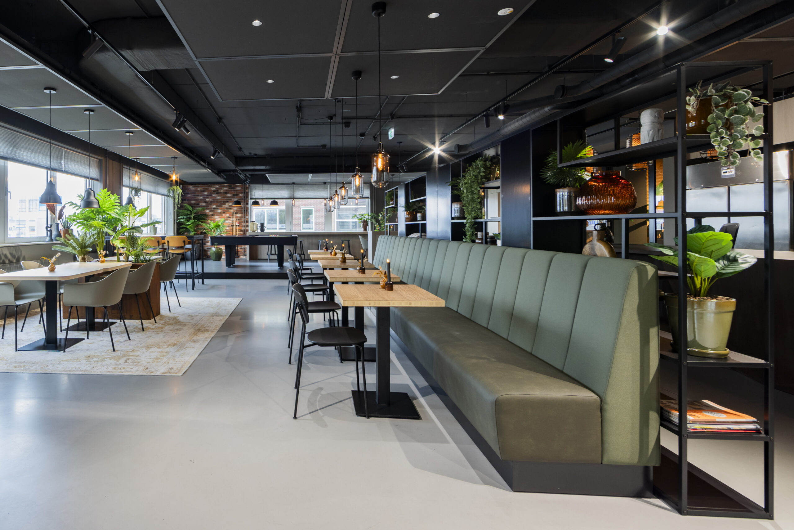 Een moderne binnenruimte met zitgedeelte, tafels en veel groen.