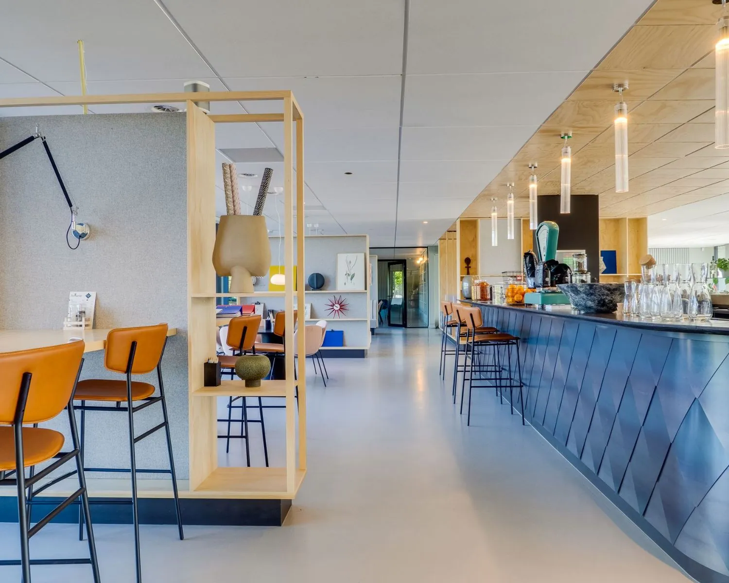 Moderne en kleurrijke kantoorcafetaria met hoge zitplaatsen, een lange bar en stijlvolle decoratie.
