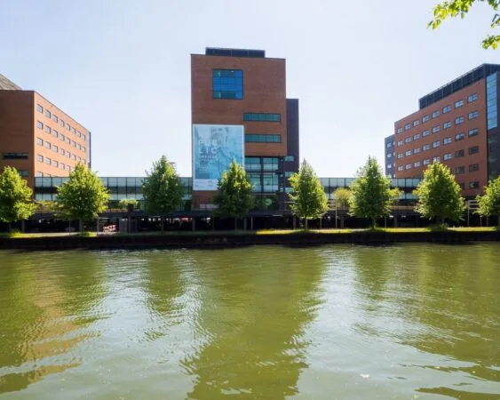 Kantoorgebouw 'The Re-.Public Offices' met bakstenen gevels aan het water, omgeven door bomen.
