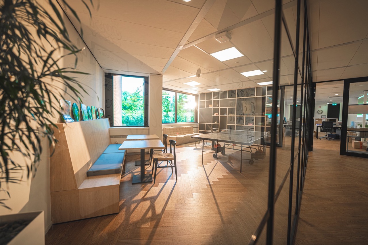 Moderne kantoorlounge met zithoek, tafeltennistafel en grote ramen die daglicht binnenlaten.