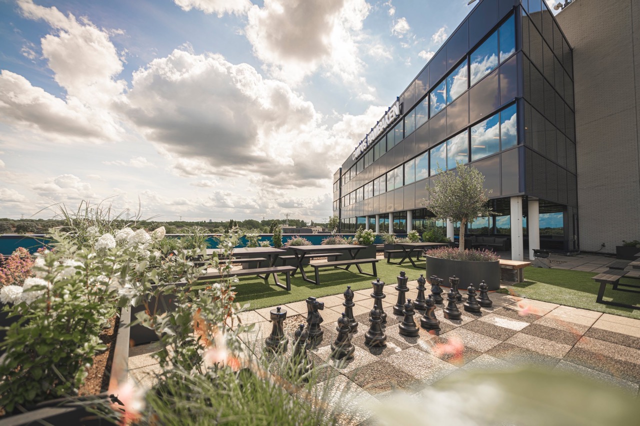 Dakterras met zitbanken, planten en een groot buitenschaakspel bij het gebouw van CBRE in een groene omgeving.