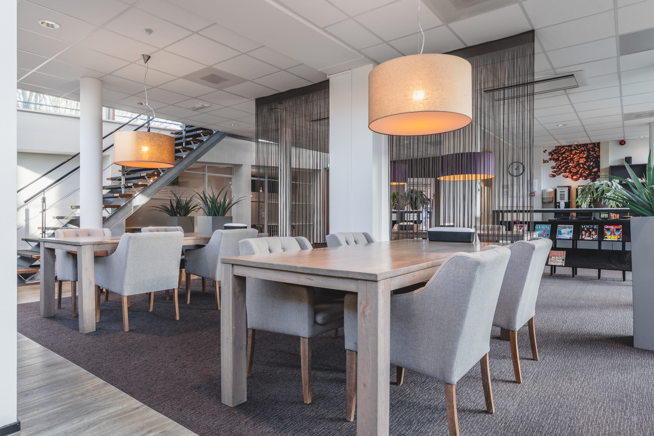 Een moderne kantoorruimte met houten tafels, grijze stoelen, en sfeerverlichting.