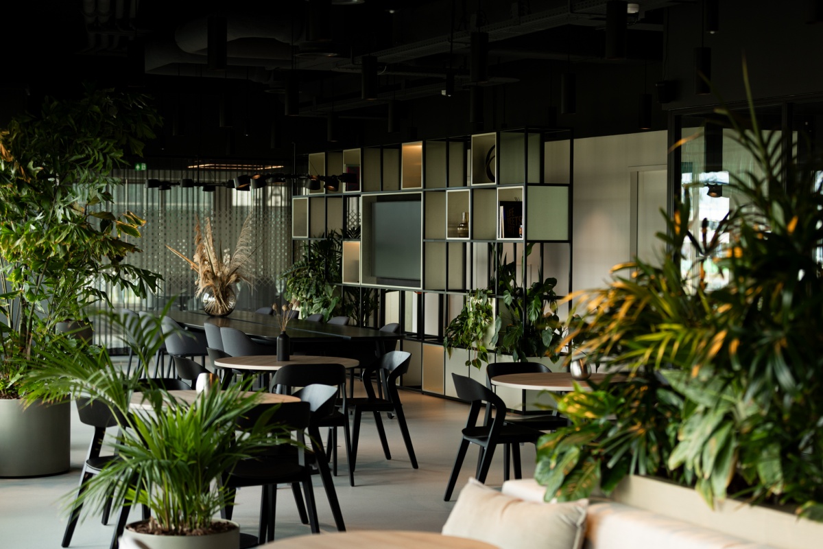 Een modern restaurantinterieur met veel groene planten en stijlvolle, zwarte meubels.