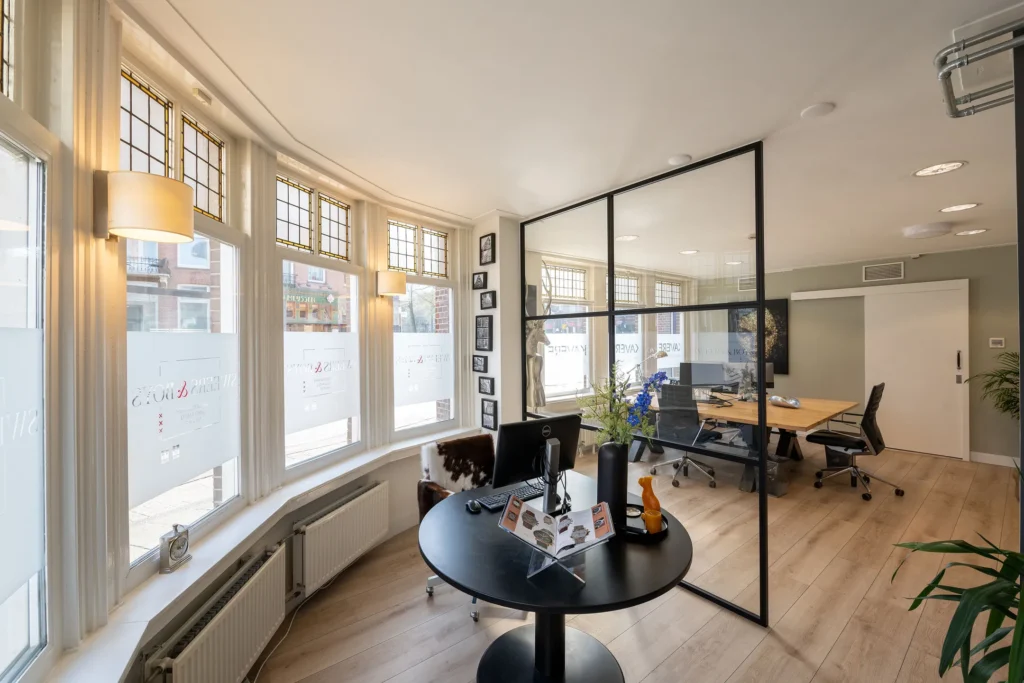 Een moderne kantoorruimte met glazen scheidingswanden en een ronde tafel bij het raam.