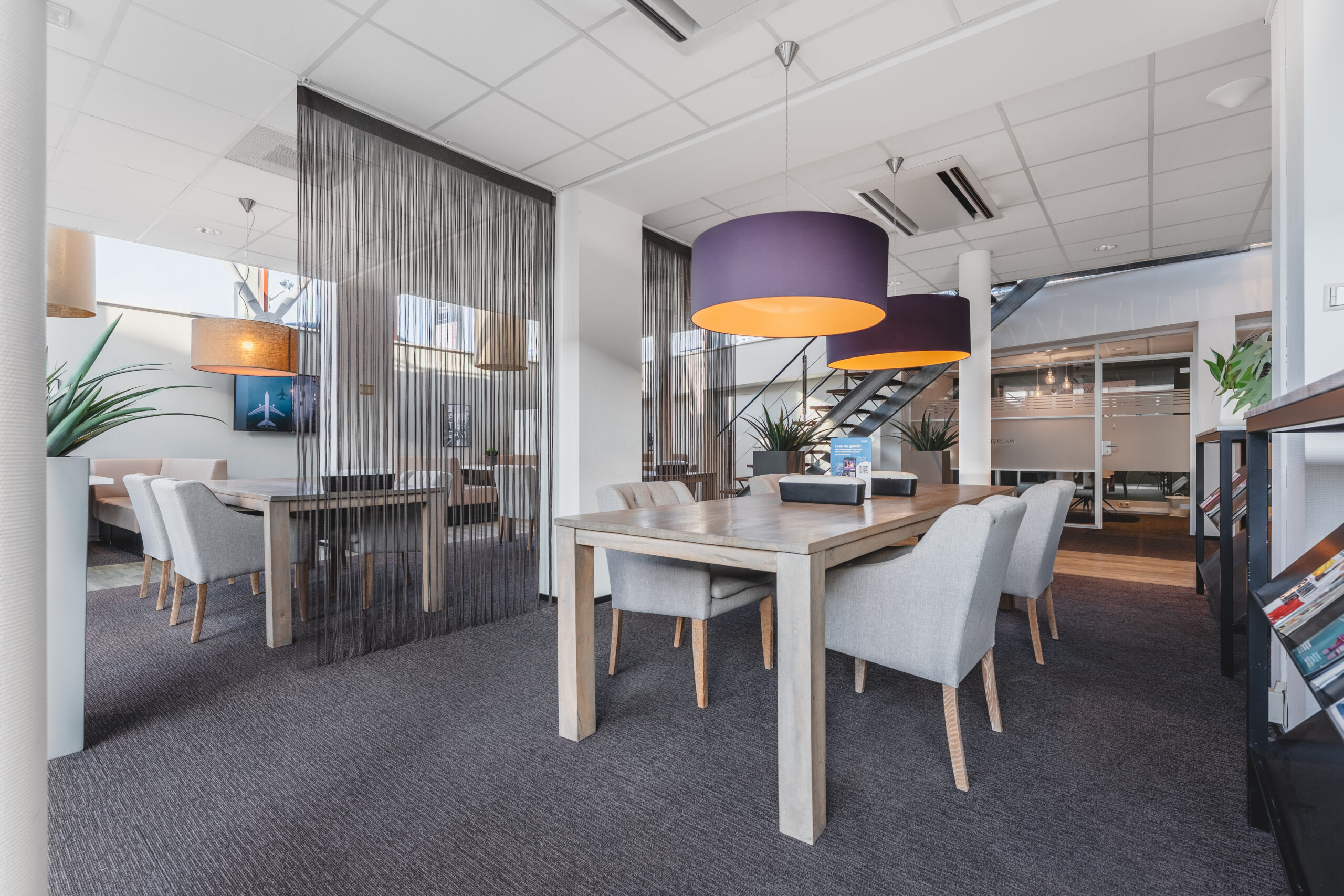 Moderne kantoorruimte met houten tafels, comfortabele stoelen en kleurrijke hanglampen.