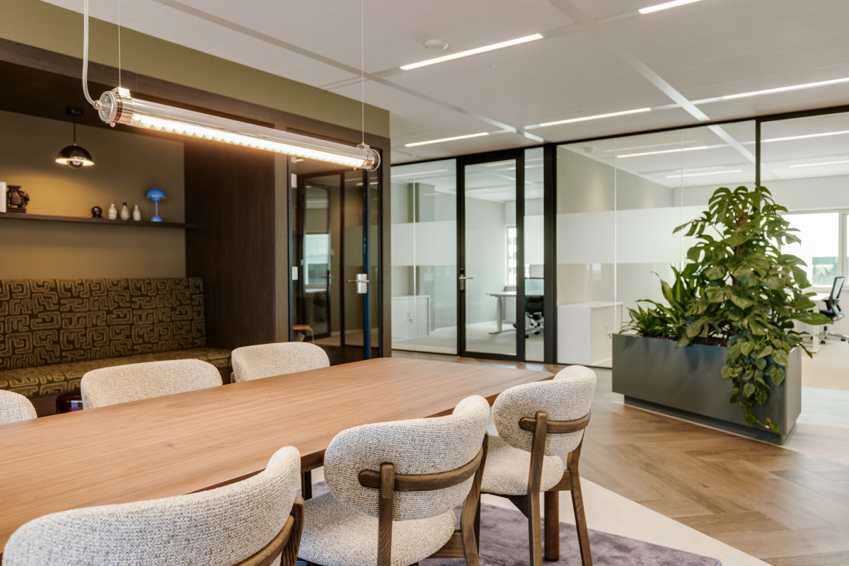 Moderne kantoorruimte met glazen wanden, een houten tafel met stoelen, en een grote groene plant.