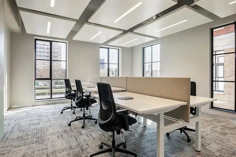 Een moderne, open kantoorruimte met bureaus en bureaustoelen bij grote ramen.