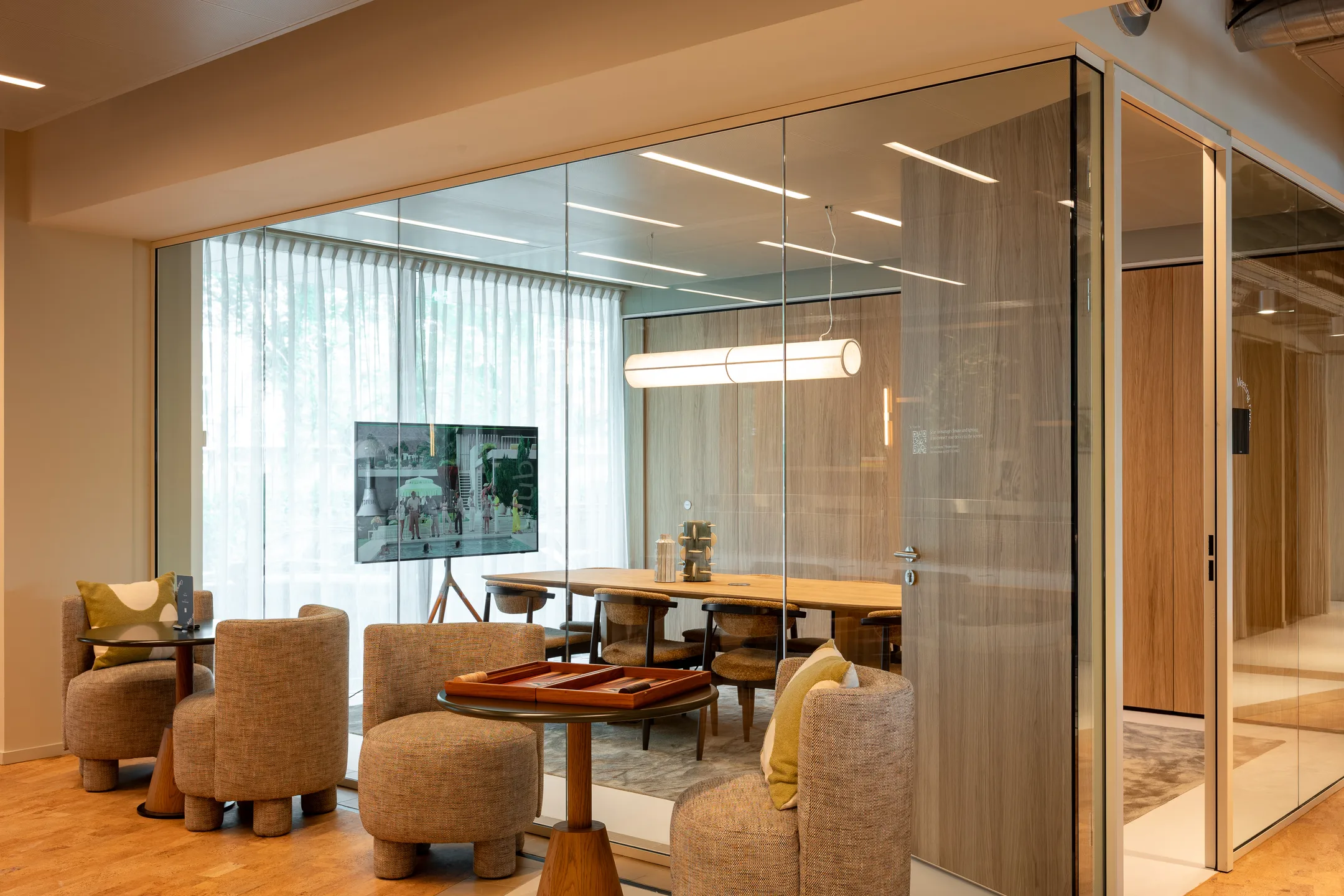 Een moderne vergaderruimte met glazen wanden, ingericht met comfortabele stoelen en een tv-scherm.
