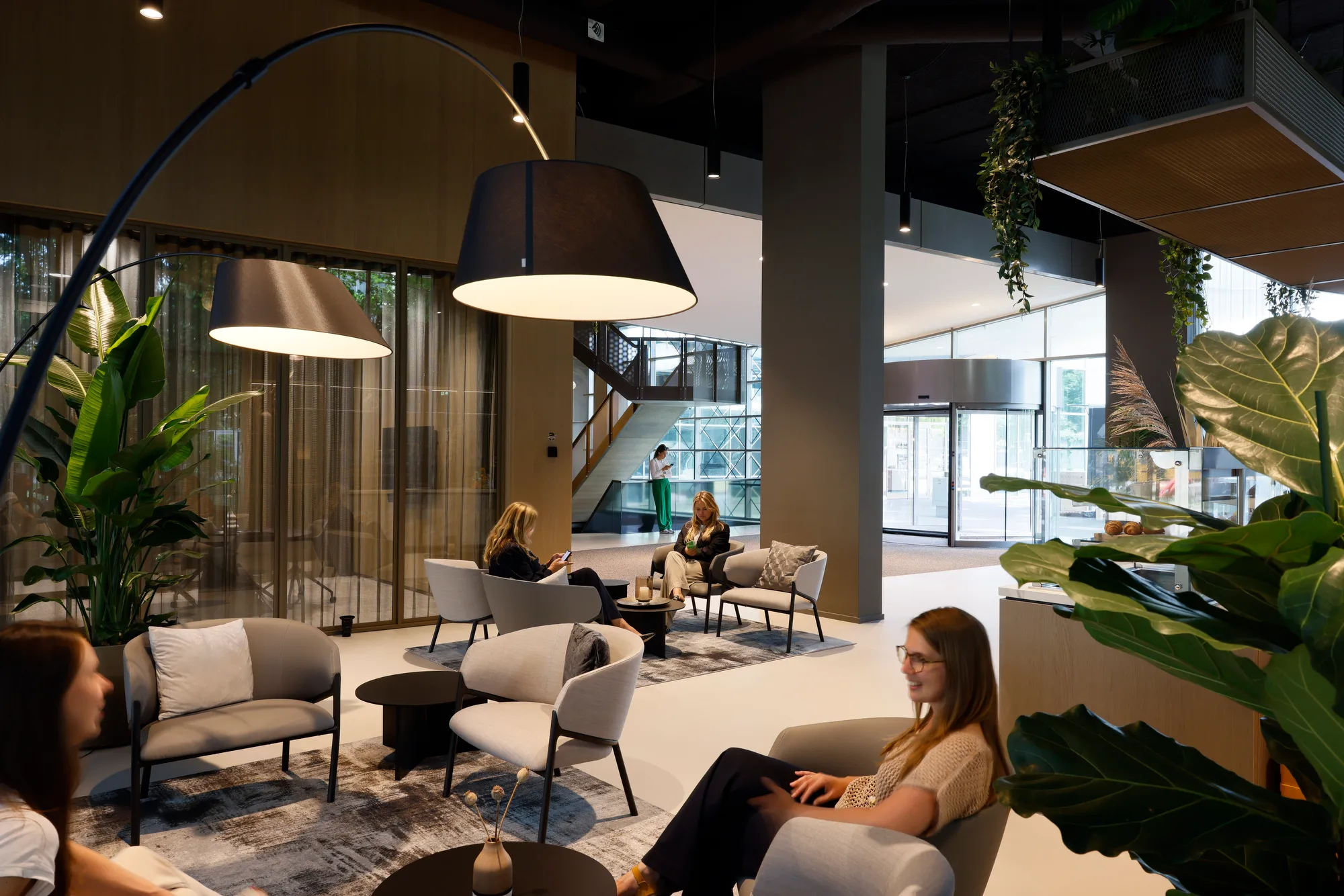 Moderne lounge met comfortabele zitplaatsen, grote hanglampen en mensen die ontspannen in een ruim, helder interieur.