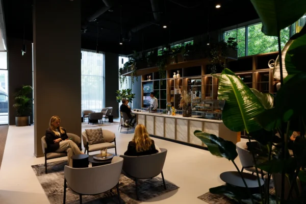 Een moderne kantoorruimte met comfortabele zitplekken en een koffiebar, omringd door grote ramen en veel groen.