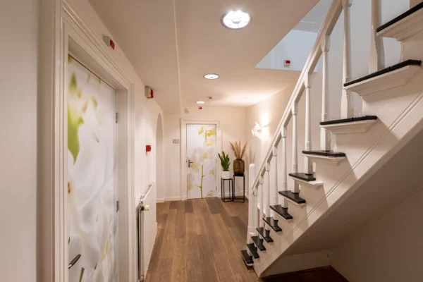 Een lichte hal met een houten vloer, een witte trap, en deuren met bloemenafbeeldingen.