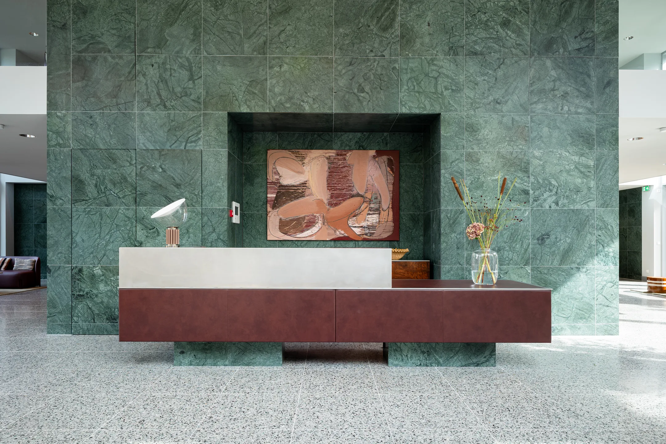 Een receptiebalie met moderne kunst aan een groene marmeren muur.