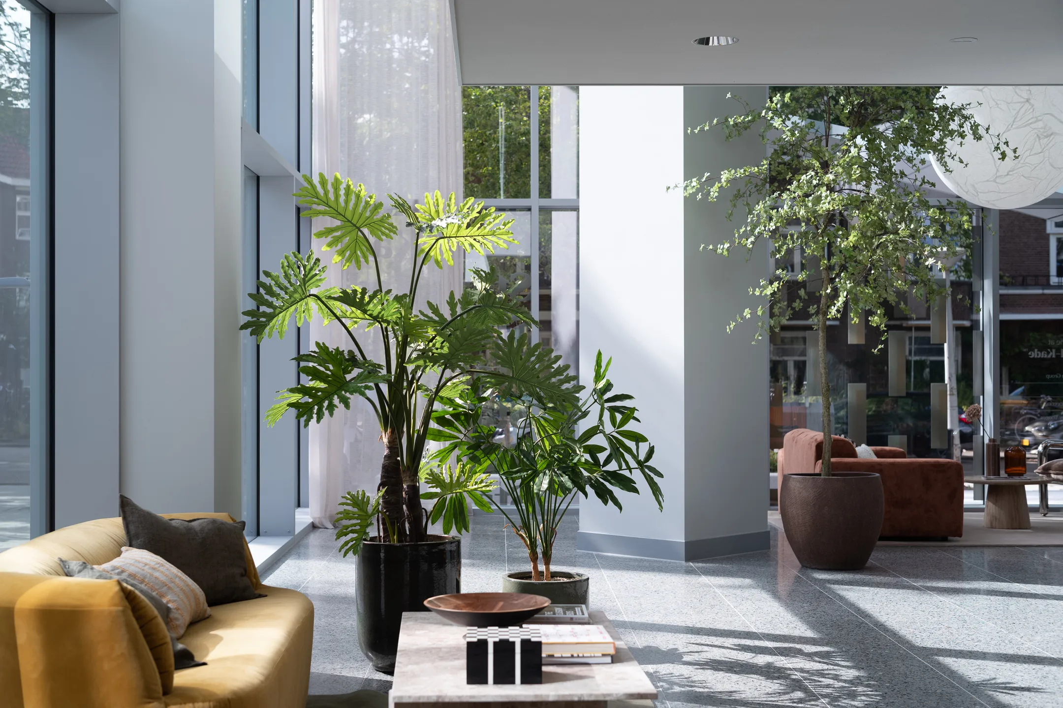Een moderne woonkamer met grote ramen, kamerplanten en een gele bank.