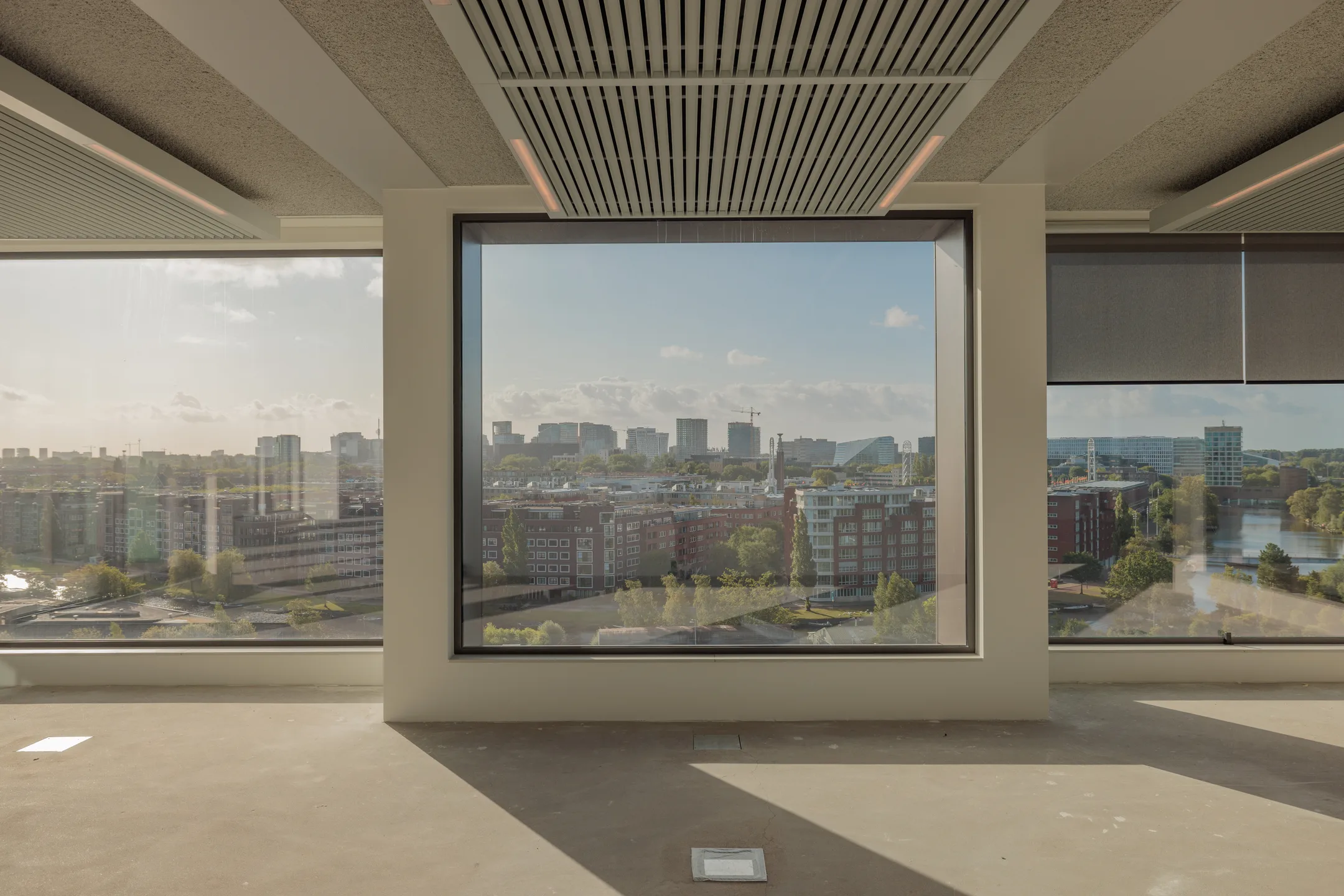 Uitzicht vanuit een leeg kantoor op een skyline met gebouwen en blauwe lucht.