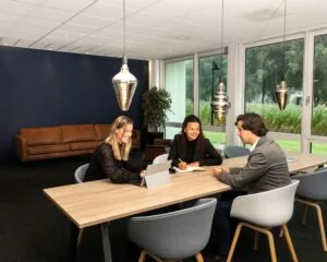 Drie mensen hebben een overleg aan een lange vergadertafel in een moderne kantoorruimte aan de Bolderweg 2a in Almere.