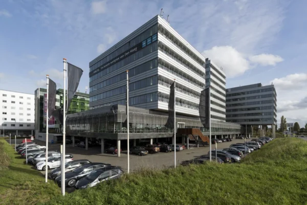 Een modern kantoorgebouw in Den Haag met parkeerplaats en vlaggen op de voorgrond.